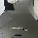 Záběr na zadní stranu černé elektrické kytary s lesklým povrchem. Jsou vidět čtyři šrouby u krku, černý plastový kryt elektroniky a v dolní části čer…