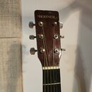 Fotografie zachycuje hlavu a horní část hmatníku akustické kytary z tmavého dřeva. Na hlavě je nápis HOHNER v bílém písmu. Jsou vidět šest kovových l…