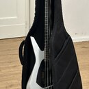 Bílá elektrická basová kytara v černém polstvu. Nástroj má bílé tělo, hnědý hmatník a černý hardware. Na hlavě je vidět nápis "Ibanez". Povrch nástro…