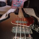 Černá elektrická basová kytara v otevřeném kufru. Nástroj má červený členitý pickguard a dva snímače, z nich pročítá nápis "D.L.I.N.E.". Povrch kytar…