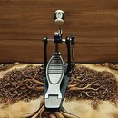 Fotografie znázorňuje jednopedálový basový pedál v černé barvě s kovovými prvky. Pedál má stříbrný šlapadlo s vodorovnými drážkami a nahoře je umístě…