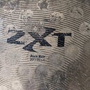 Detailní záběr na povrch kovového činele s výrazným žebrováním. Uprostřed je černý nápis ZXT a pod ním text Rock Ride 20" / 51cm. Povrch vykazuje zna…