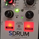 Bílý efekt pedál s nápisy GROOVE, KIT a HATS/RIDES. Na zařízení je vidět velké logo SDRUM a text Strummable Drums™. Obsahuje dva černé otočné knoflík…