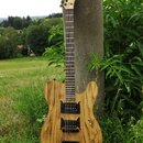 Elektrická kytara s přírodním dřevěným povrchem s výraznou sletovanou strukturou. Na hlavě hmatníku je nápis "Custom". Nástroj má dva černé humbucker…