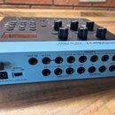 Modře a černý elektronický modul s nápisy Roland, TM-6 PRO a TRIGGER MODULE. Na zadní straně jsou konektory s popisky FOOT SW, HH CTRL, TRIGGER IN 1–…