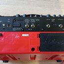 Zadní strana červeného přenosného komba s černými ovládacími prvky. Na zařízení jsou nápisy DC IN, USB, LOOPER/GUITAR/MIC, HARMONY/MIC/INST, PHONES/R…