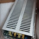 Stříbrný kovový šasi s perforovaným horním krytem v podobě ventilačních mřížek. V otevřené spodní části jsou vidět elektronické součástky, žluté kone…
