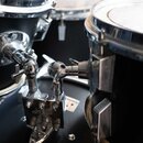 Detailní záběr na části černé bicí soupravy s chromovaným hardwarem. Jsou vidět části dvou bubnů, držáky a spojovací ramena s utahovacími šrouby. Pov…