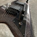 Elektrická kytara s tělem ve tvaru V a tmavým třpytivým povrchem. Nástroj má dva černá humbuckery, černý plech s dvěma otočnými knoflíky a jedním pře…