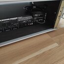 Zadní strana černého elektronického zařízení umístěného v hliníkovém racku. Jsou zde viditelné nápisy OUTPUT 1 L-BALANCED-R, OUTPUT 2 FX SEND, XLR GR…