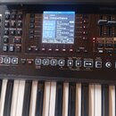 Černý digitální klavír značky Roland. V horní části je displej s modrým podsvícením, na kterém je text Dance 141 CrossovrDance a seznamy zvuků jako C…