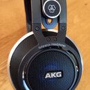 Detailní pohled na černá otevřená sluchátka s kovovými prvky. Na vnější straně mušle je nápis Reference Headphones a logo AKG. Dole na rámu je uveden…