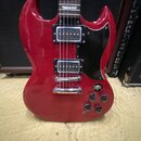 Červená elektrická kytara s černým pickguardem a dvěma humbuckery. Na krku jsou vidět trapezoidní vložky. Tělo vykazuje drobné oděrky a známky použív…