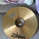 Zlatý kovový činel s viditelnou strukturou kování. Na povrchu je černý nápis Zildjian a v horní části šedý obdélníkový štítek. Uprostřed na kopuli je…