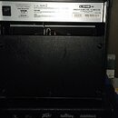 Fotografie zachycuje zadní stranu dvou černých kytarových komb. Horní přístroj má štítek s nápisy LINE 6, SPIDER IV 15 AMPLIFIER - 15 WATTS 1X8 a sér…