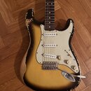 Elektrická kytara s tvarem Stratocaster, trojbarevným sunburst lakem a bílým pickguardem. Tělo vykazuje výrazné opotřebení v podobě rozestřeného laku…