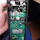 Fotografie zachycuje otevřený černý plastový kryt elektronického zařízení s viditelným zeleným plošným spojem. Na desce jsou rozmístěny součástky, po…