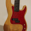 Pětstrunová elektrická basová kytara s přírodním dřevěným povrchem těla a hmatníkem z tmavého dřeva. Nástroj má červený pickguard s mramorovým vzorem…