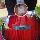 Černá akustická kytara s cutawayem a červeným přechodem (sunburst) na spodní části korpusu. Povrch je vysoce lesklý s viditelnou strukturou dřeva v č…