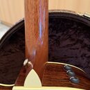 Detailní pohled na spoj hmatníku a krku akustické kytary s tmavým dřevěným povrchem. Na hranici krku a korpusu je vidět bílý trojúhelníkový vložkový…