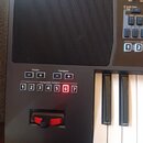 Detailní pohled na ovládací panel černého klávesového nástroje. Jsou zde vidět tlačítka s nápisy Octave (- +), Transpose (- +) a řada Assignable Swit…