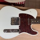 Bílá elektrická kytara typu Telecaster s tmavě hnědým pickguardem zvláště s texturou želvy. Na kovovém krytu snímače je nápis "MADE IN USA". Tělo vyk…
