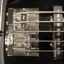 Detailní pohled na chromovaný kobylku basové kytary s nápisem FENDER. Pod kobylkou je umístěn černý snímač s bílým nápisem Seymour Duncan. Povrch kov…