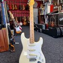 Elektrická kytara typu Stratocaster v krémové barvě s bílým pickguardem a hnedým javorovým hmatníkem. Na hlavě je vidět nápis Fender. Kytara má tři s…