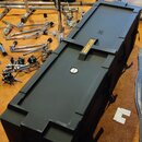 Černý obdélníkový přepravní kufřík z plastu s nápisem HARDCASE a logem v kruhu. Kufřík má na horní straně kulatý zámek a boční úchytky. V pozadí jsou…