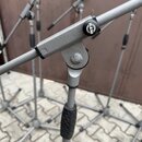 Detailní záběr na kovový mikrofonový stojan stříbrné barvy. Na černém plastovém knoflíku je bílý nápis K&M. Povrch kovu vykazuje drobné známky opotře…