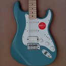 Modře lakovaná elektrická kytara typu Stratocaster s bílým pickguardem a světle hnědým javorovým hmatníkem. Na bílém plastu je nalepený červený kulat…