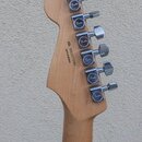 Zadní strana hlavy kytary z přírodního dřeva s šesti chromovanými ladičkami. Na každém knofíku ladičky je nápis Fender. Na dřevě je vyryto MADE IN ME…