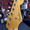 Záběr na hlavu kytary z přírodního světlého dřeva. Na povrchu je černý nápis Fender a STRATOCASTER, v horní části menší text ORIGINAL Contour Body. J…