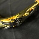Detailní záběr na část zlatého dechového nástroje s černými kovovými klapy. Na jedné z klap je vyryto kulaté logo značky Yamaha. Povrch nástroje je l…