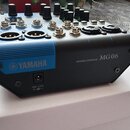 Kompaktní míchací pult černé barvy s modrým pruhem na přední straně. Na zařízení je uveden nápis YAMAHA s logem a označení MIXING CONSOLE MG06. Horní…