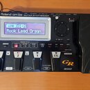 Černý kytarový syntetizátor s nápisem Roland GR-55 GUITAR SYNTHESIZER. Zařízení má digitální displej, na kterém je text LEAD 01-2 Rock Lead Organ, ně…