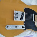 Žlutá elektrická kytara typu Telecaster s černým pickguardem a javorovým hmatníkem. Na kovovém krytu snímače není žádný viditelný nápis ani logo. Pov…