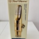 Fotografie znázorňuje krabičku s nápisy Theo Wanne™, TRUE LARGE CHAMBER a Made in USA. Uprostřed je vyobrazen zlatý kovový mouthpiece s logem ve tvar…