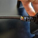 Detailní záběr na poškozený černý kabel u připojení k zařízení. Vnější izolace je přetrhaná a jsou vidět vnitřní vodiče v červené a žluté barvě. Kabe…