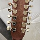 Fotografie zachycuje hlavu twelve-string kytary z hnědého dřeva s dvanácti zlatými ladicími mechanismy. Na horní hraně je vyryt nápis RICHWOOD GUITAR…