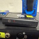 Černý obdélníkový bezdrátový vysílač s nápisy VOLUME, OUTPUT a POWER/PAR. Na horní straně je bílý oválný štítek s textem ROCKY WIRELESS SYSTEM a žlut…
