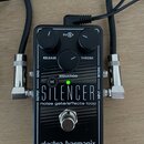 Černý efekt pedál s nápisy THE SILENCER a noise gate/effects loop. Na zařízení jsou tři ovládací knoflíky s popisky RELEASE, THRESH a REDUCTION, vstu…