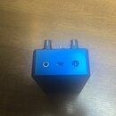 Modrý kovový přístroj s anodyzovaným povrchem. Na přední straně jsou tři konektory: jack vstup, USB-C port a další kulatý konektor. Horní strana obsa…