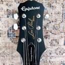 Černý hlavník elektrické kytary s nápisy Epiphone, Les Paul SPECIAL a Vintage Edition. Nástroj má šest chromovaných ladiček a stříbrné vrchovky strun…