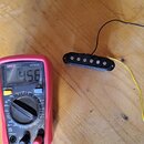 Na dřevěném povrchu leží černý elektrický snímač s šesti viditelnými polosférickými póly a dvěma připojenými vodiči, žlutým a černým. Vedle něj je če…