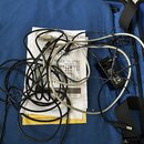 Na modrém textilním povrchu leží bílý papírový návod s nápisy LineTrack a ZOOM, černý napájecí adaptér a několik kabelů v bílé a černé barvě. Na adap…
