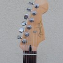Detail hlavy kytary z přírodního dřeva s šesti chromovanými ladičkami. Na povrchu je černý nápis "Fender" a menší svislý text "DUO SONIC". Hrabednice…