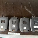 Čtyři černé bezdrátové vysílače značky SHURE, model SLXD1. Každý kus má v horní části anténu a v dolní části slot pro baterie. Na předních stranách j…
