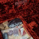 Interiér tvrdého kufru s červeným plyšovým polstřením. Na víku je nápis Fender 70th Anniversary STRATOCASTER 1954 - 2024. V kufru se nachází sada pří…