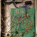Fotografie zachycuje vnitřek kovového šasi s elektronickými součástmi. Uprostřed je zelená tiskovaná spoje s rozváděcími cestami, na které jsou připá…